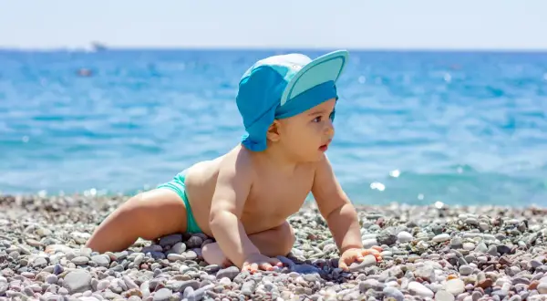 Un bimbo con cappellino blu esplora la spiaggia, curioso del mare. Un'immagine di neonati al mare che cattura la meraviglia.