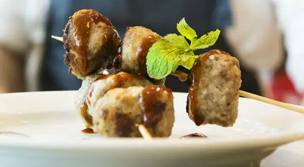 Spiedini di polpette di fagioli, condite con salsa e guarnite con menta fresca, su un piatto bianco.