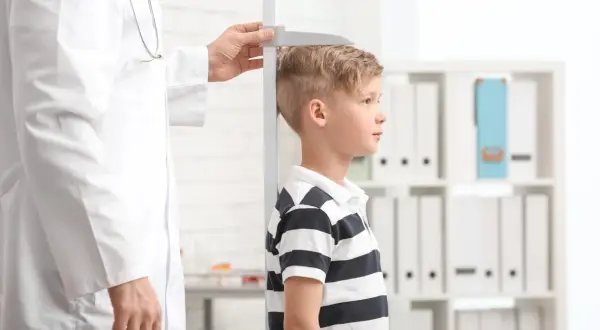Un bambino viene misurato da un medico. La domanda "quanto sarà alto mio figlio" aleggia nell'aria mentre si attende il risultato.