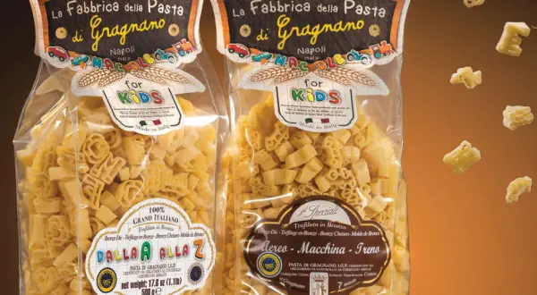 Due confezioni di pasta per bambini, una con lettere e l'altra con aerei, macchine e treni, prodotte a Gragnano.