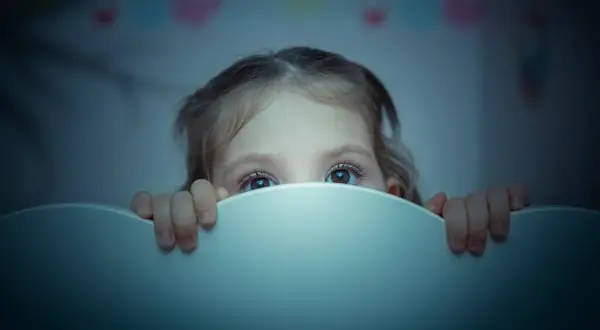 Occhi spaventati di un bambino di 2 anni che si sveglia piangendo disperato nel buio.