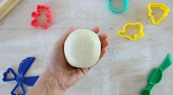 Mano che tiene una palla di pasta di sale, pronta per creare forme con stampini colorati e attrezzi. Ricetta facile per divertirsi.
