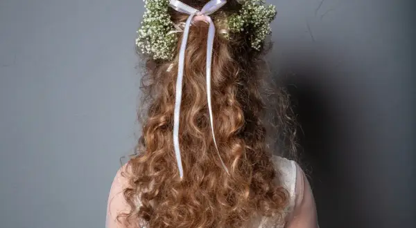 Capelli ricci con coroncina di fiori e nastri, perfetti per trecce acconciature comunione.