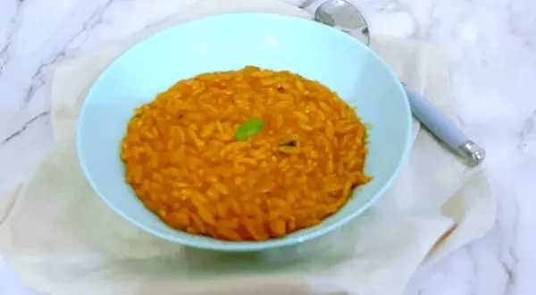 Un piatto di pastina al pomodoro, gustosa e profumata, guarnita con una fogliolina verde.