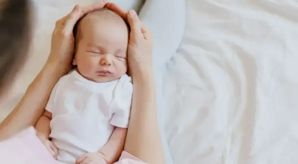 Mani che accarezzano la testa di un neonato addormentato. Il dolce rumore phon bambini lo culla nel sonno.