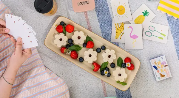 Picnic per bambini con panini a forma di fiore, fragole, mirtilli e carte da gioco colorate.