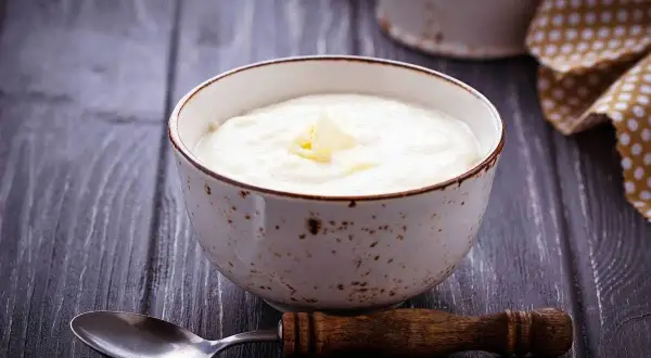 Una ciotola di semolino dosi per 1 persona con latte, guarnita con un pezzetto di burro. Un cucchiaio di legno è appoggiato accanto.