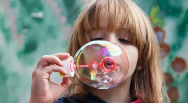 Bambina soffia bolle di sapone iridescenti. Una ricetta veloce per un momento di gioia.