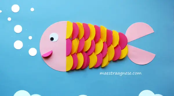 Pesciolino colorato creato con lavoretti per bambini in estate. Bollicine e onde di carta completano la scena marina.