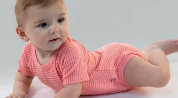 Un adorabile neonato di 7 mesi, sdraiato a pancia in giù, indossa un body a righe corallo.
