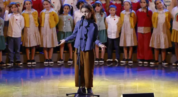 Una bambina canta sul palco, circondata da un coro di bambini, un momento che ricorda le 25 canzoni più famose dello Zecchino d'Oro.