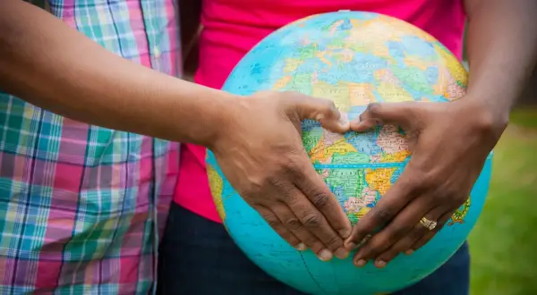 Mani a forma di cuore circondano un globo, simbolo del desiderio di adottare un bambino e accoglierlo nel mondo.