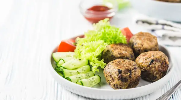 Polpette lenticchie e patate dorate, servite con insalata fresca, pomodoro e cetrioli a spirale. Un piatto gustoso e salutare.