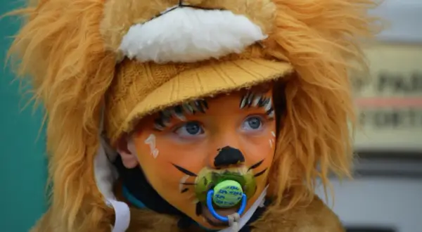 Bambino con trucco carnevale facile da leone, con ciuccio e cappello giallo.
