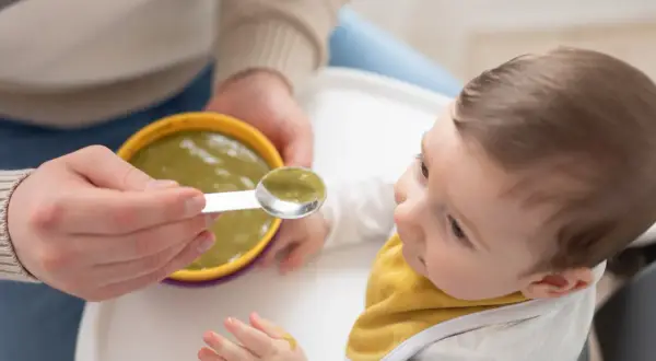 Bambino curioso assaggia la sua prima pappa svezzamento, con un cucchiaino pieno di verdure.