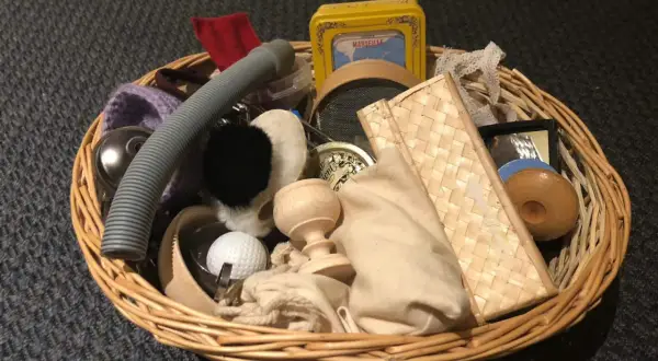 Un cestino dei tesori pieno di oggetti curiosi: un tubo grigio, una pallina da golf, un piccolo specchio, una scatola gialla e altri elementi da esplorare.