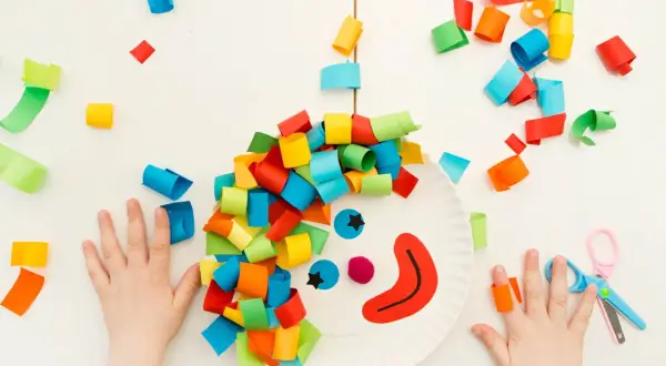 Bambini creano un clown con carta colorata, un'idea per giochi di carnevale. Ritagli di carta colorata e forbici.