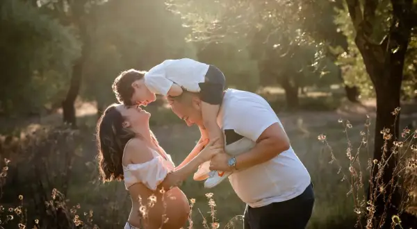 Una bellissima giornata della famiglia, con un bimbo sulle spalle del papà che bacia la mamma in dolce attesa, immersi nella luce dorata del tramonto.