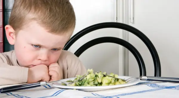 Bambino con espressione di disgusto davanti a un piatto di purè e verdure. Il suo volto mostra un riflesso di estrusione, come se volesse fuggire da quel cibo.