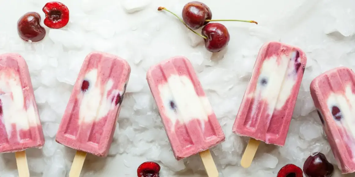 Ghiaccioli fatti in casa con ciliegie e yogurt, su un letto di ghiaccio tritato. Freschi e invitanti, perfetti per l'estate.