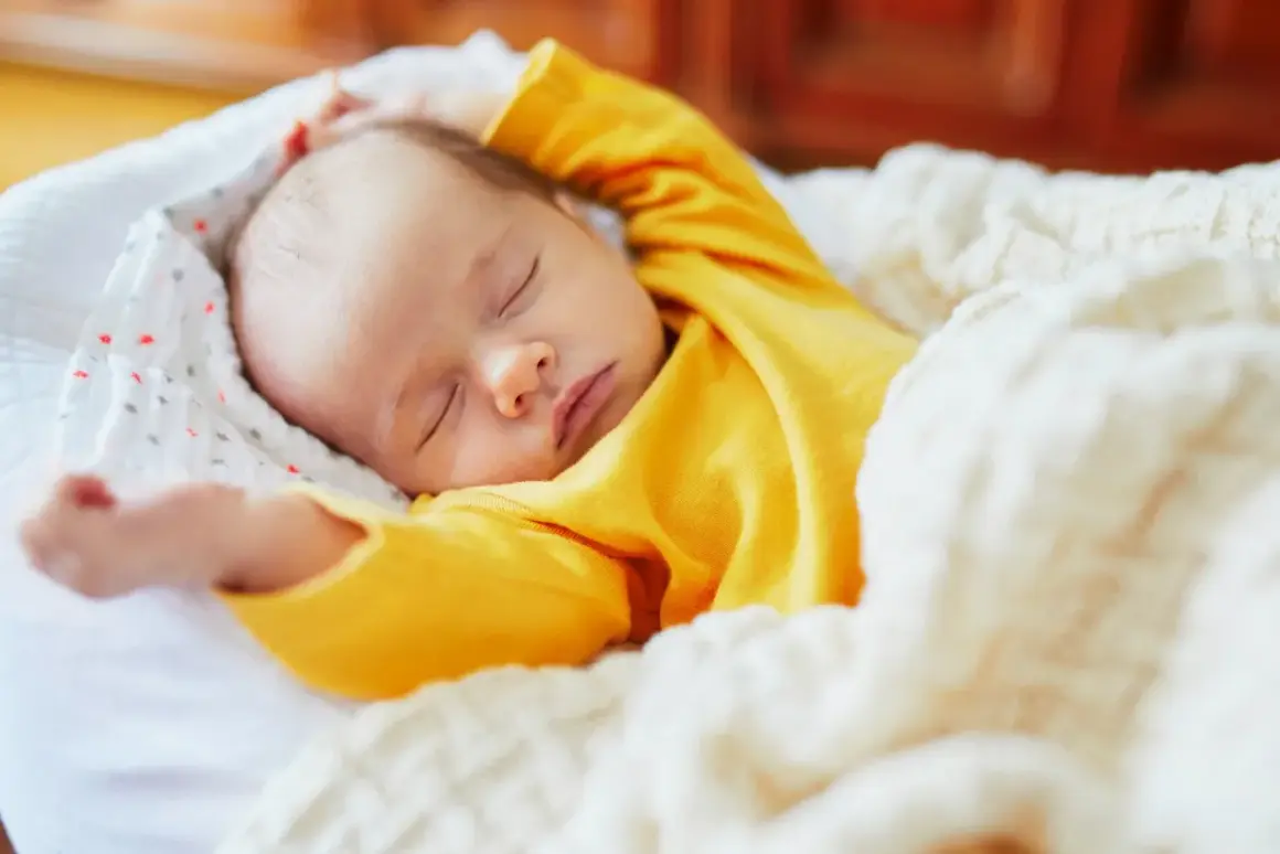 Dolce neonato piange nel sonno, avvolto in una coperta calda. Le sue braccia sono sollevate, come in un sogno agitato.