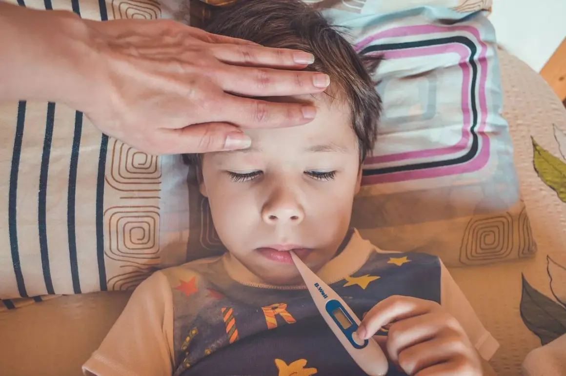Bambino con febbre, mano sulla fronte, termometro in bocca. Possibili sintomi streptococco bambini.