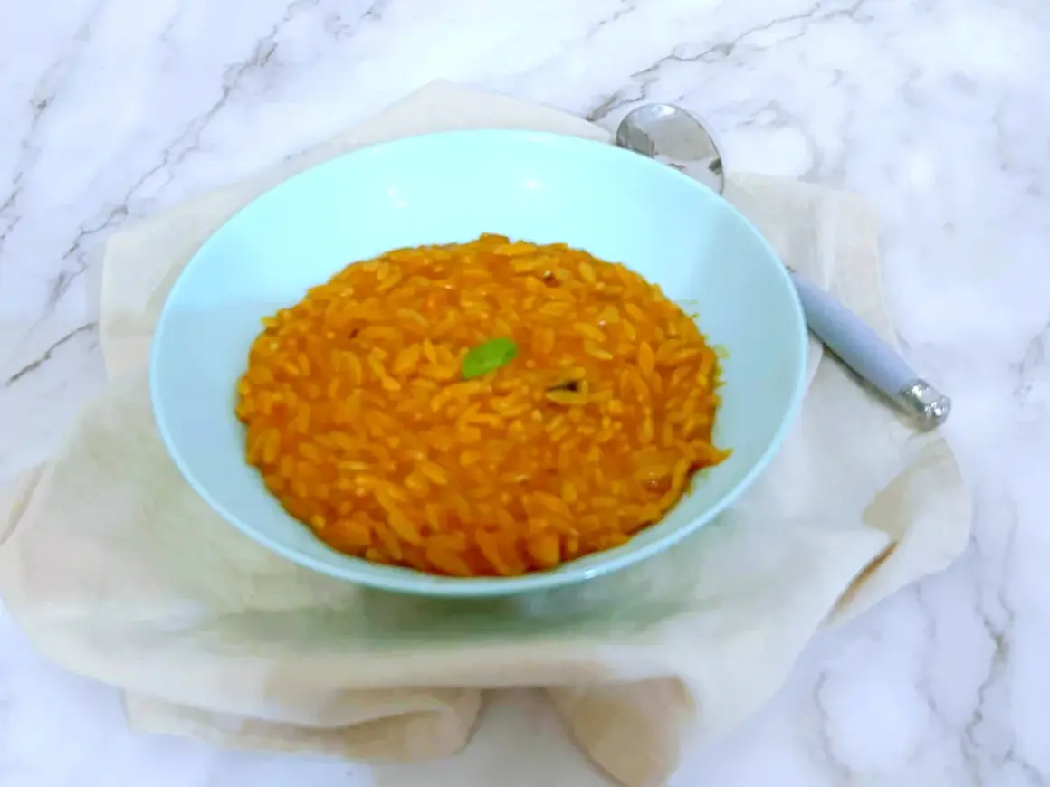Un piatto di pastina al pomodoro, gustosa e profumata, guarnita con una fogliolina verde.