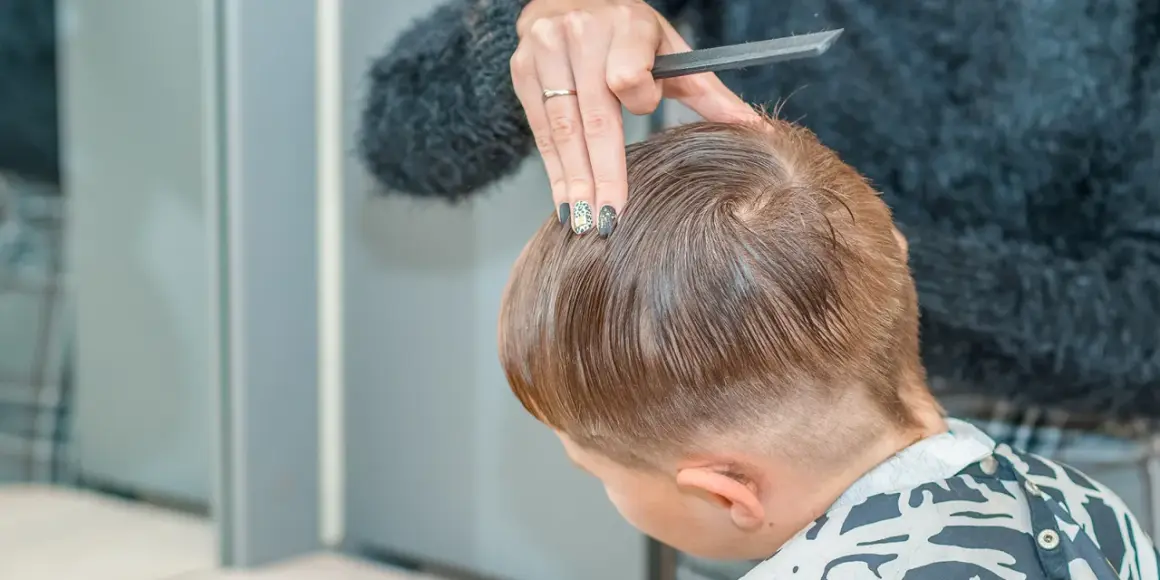 Mani esperte creano un nuovo taglio capelli bambino maschio, pettinando e rifinendo con cura.