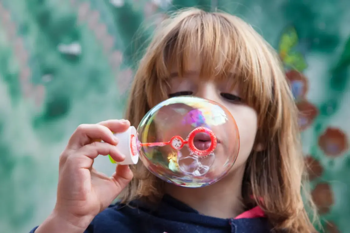 Bambina soffia bolle di sapone iridescenti. Una ricetta veloce per un momento di gioia.