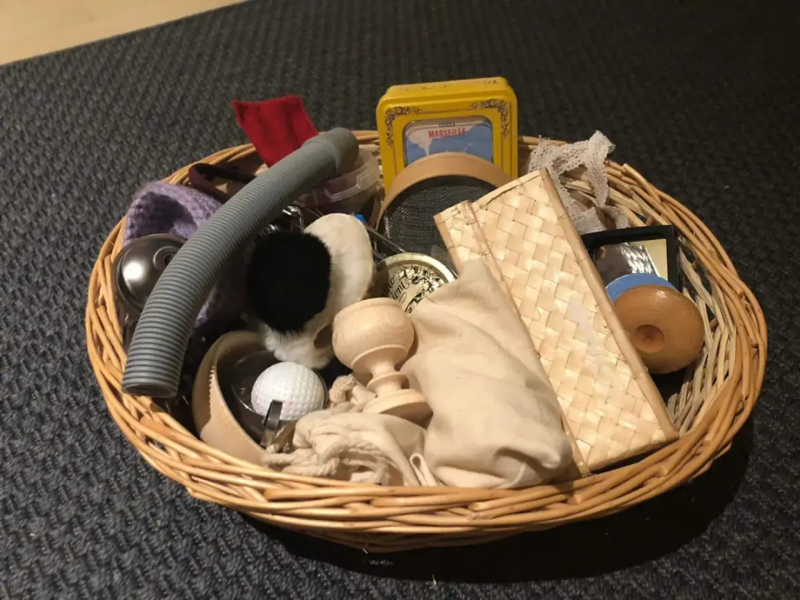 Un cestino dei tesori pieno di oggetti curiosi: un tubo grigio, una pallina da golf, un piccolo specchio, una scatola gialla e altri elementi da esplorare.