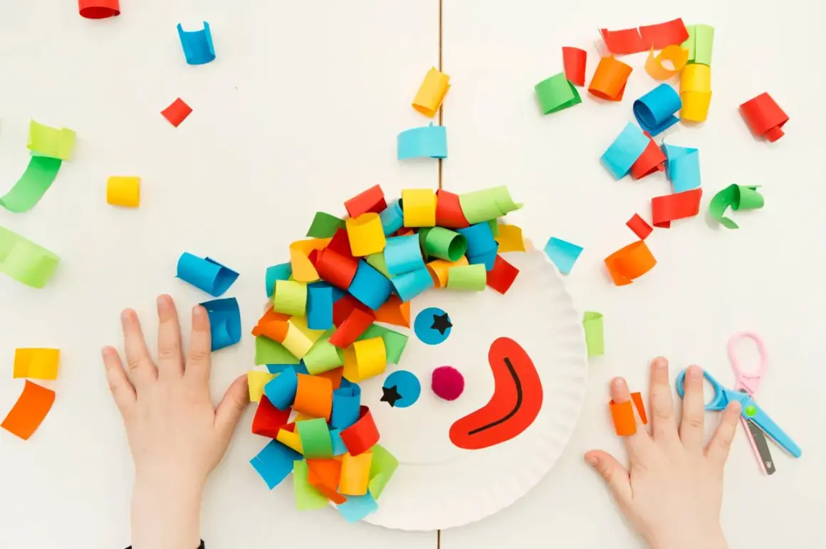 Bambini creano un clown con carta colorata, un'idea per giochi di carnevale. Ritagli di carta colorata e forbici.