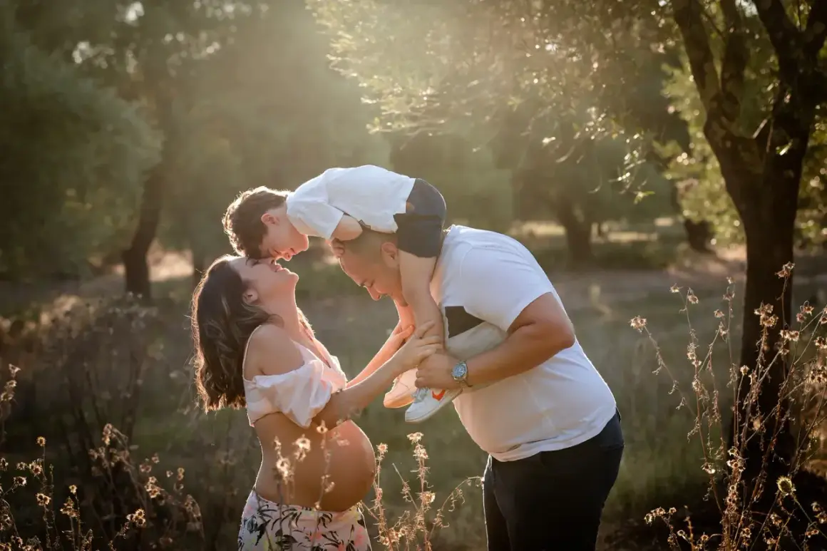 Una bellissima giornata della famiglia, con un bimbo sulle spalle del papà che bacia la mamma in dolce attesa, immersi nella luce dorata del tramonto.