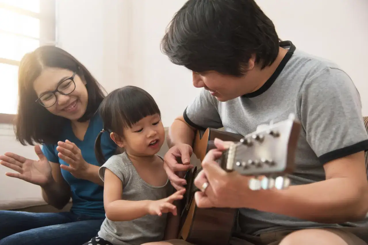 Famiglia felice che suona la chitarra, creando canzoni dedicate ai figli. La mamma batte le mani, il papà insegna alla bimba.