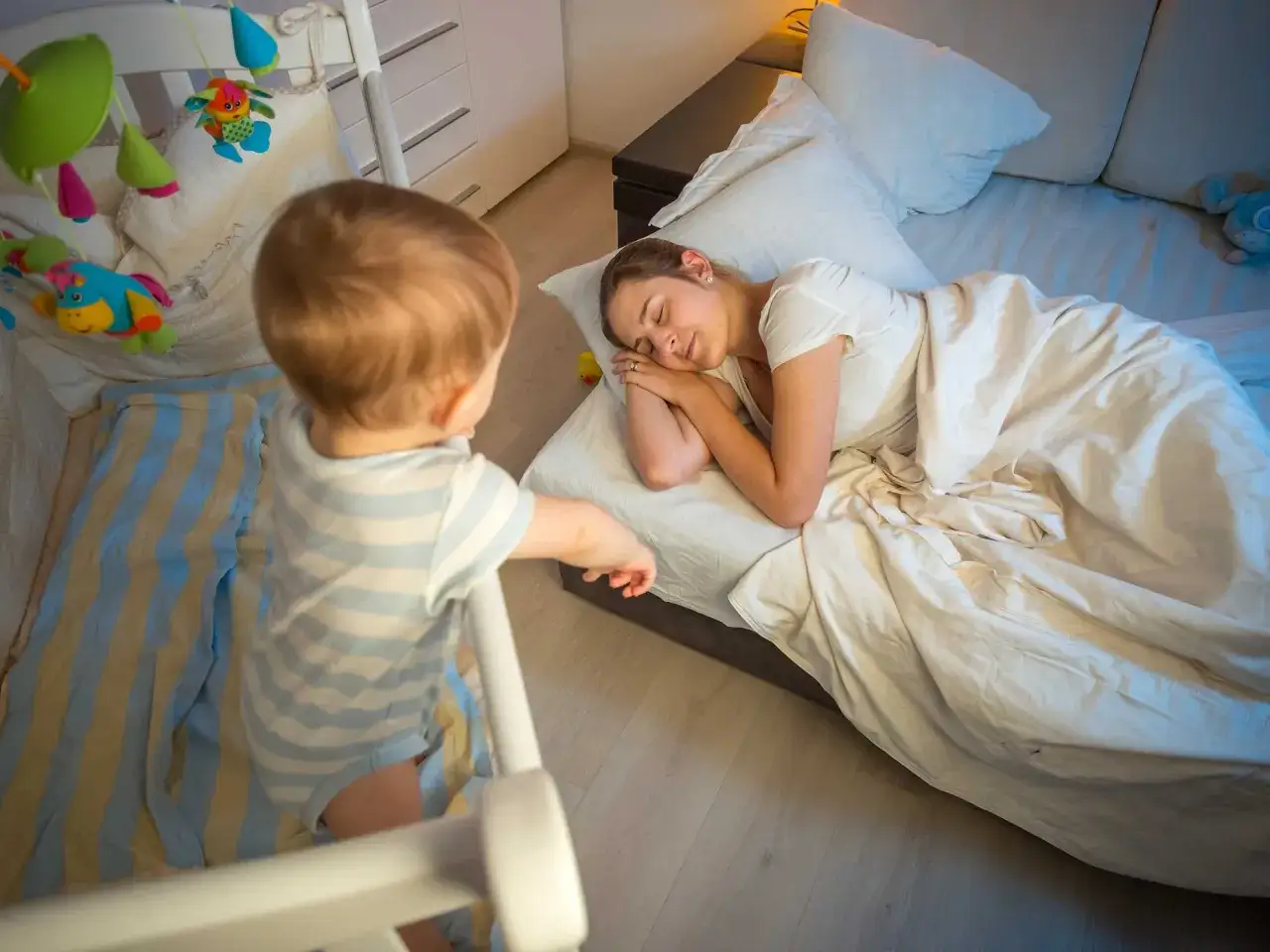 Bambino in culla osserva la mamma addormentata, forse un momento di regressione del sonno per entrambi.