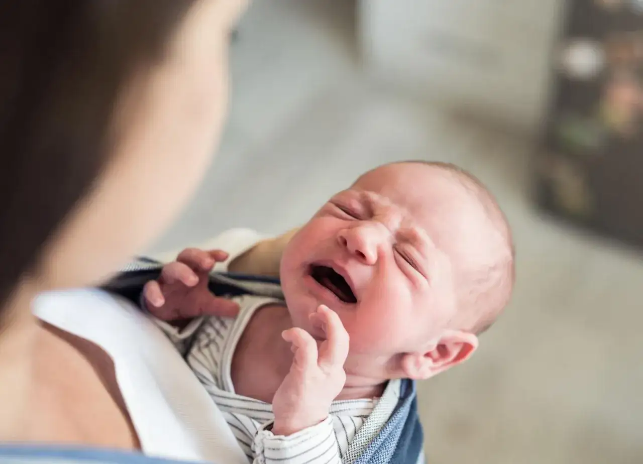 Neonato di 6 mesi con urla acute, viso arrossato e occhi chiusi. Le manine si agitano.