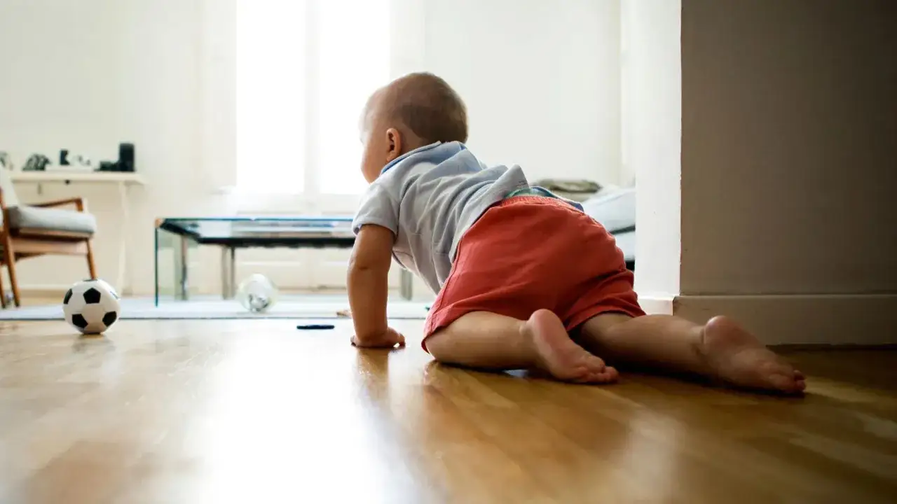 Bambino gattona sul pavimento in legno, pronto a esplorare. A quanti mesi si gattona? Ogni bimbo ha i suoi tempi!