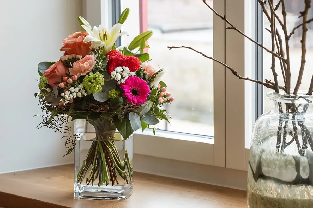 Un colorato bouquet di fiori, perfetto per la festa della mamma, in un vaso di vetro su un davanzale.