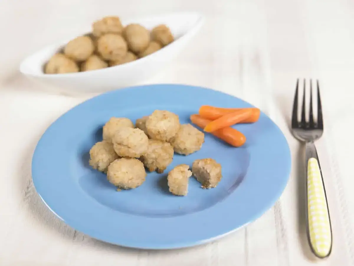 Deliziose polpette di pesce per bambini, dorate e croccanti, servite su un piatto azzurro con carotine.