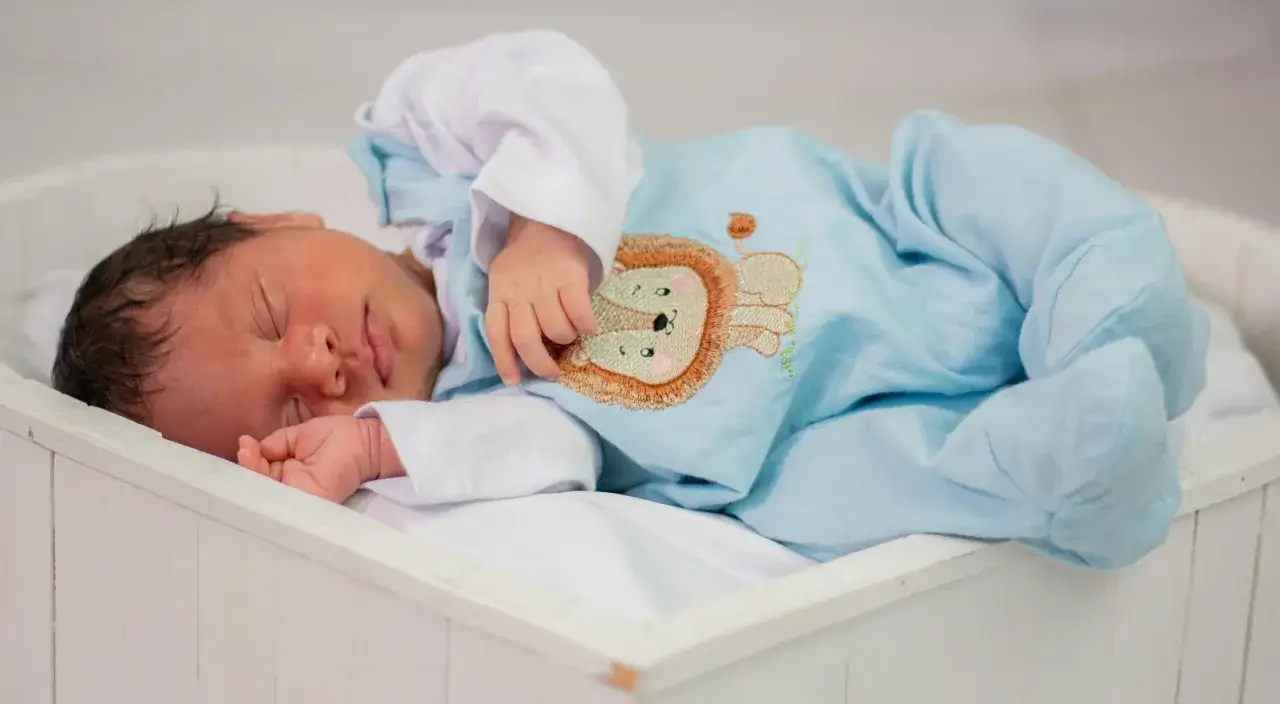 Dolce neonato di 3 mesi dorme sereno in una culla, vestito con un pigiamino azzurro con un simpatico leoncino ricamato.