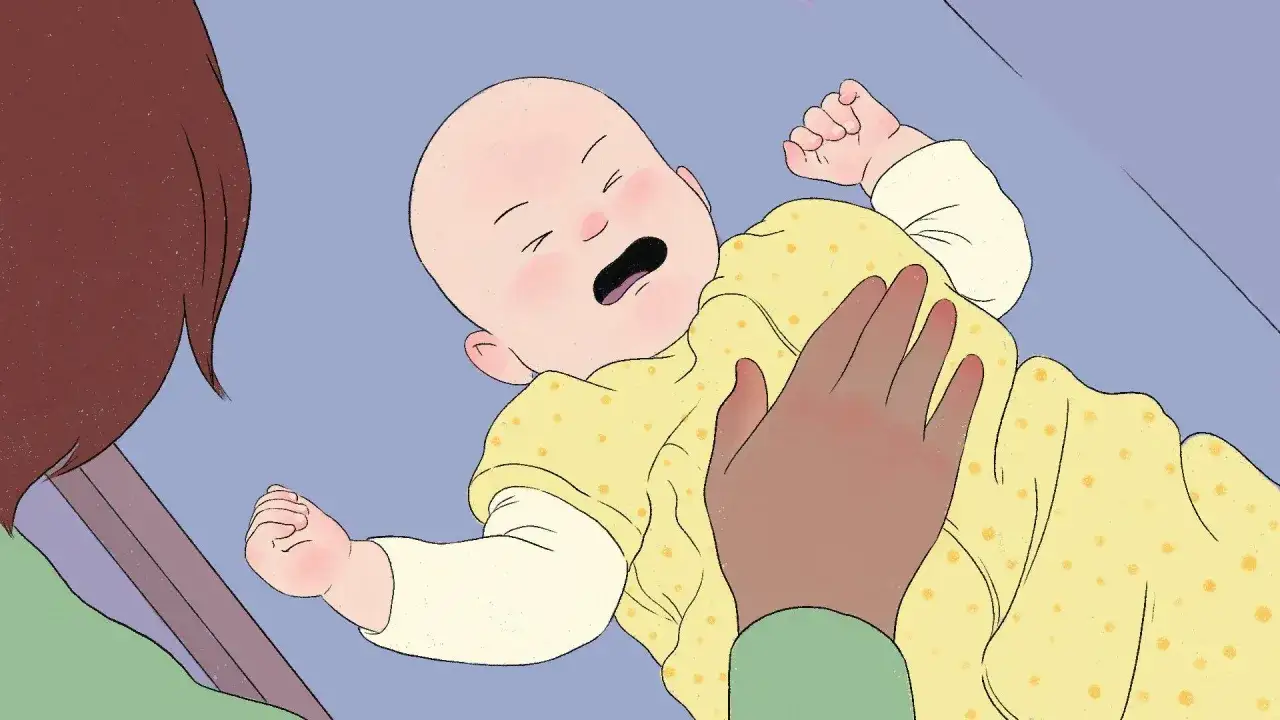 Un neonato piange nel sonno, avvolto in una copertina gialla a pois. Una mano lo accarezza dolcemente.