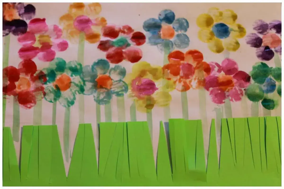 Fiori colorati con impronte di dita, un'idea per lavoretti per bambini. L'erba verde ritagliata completa il disegno.