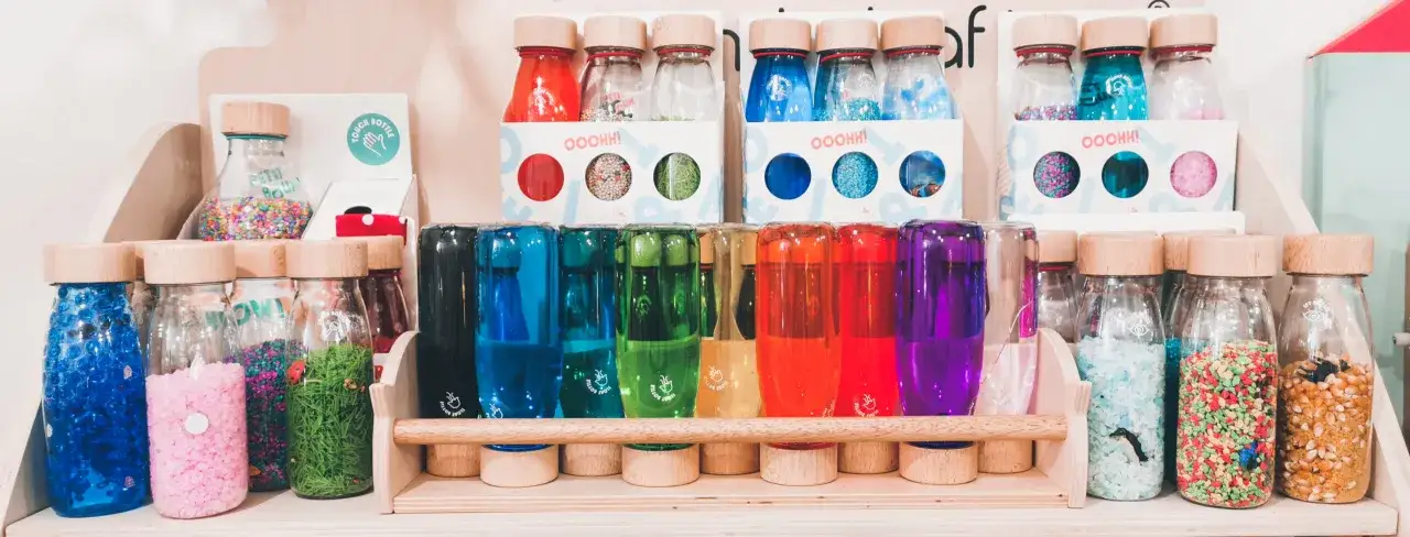 Una fila di barattoli della calma colorati, pieni di glitter, perline e elementi naturali, pronti a incantare.