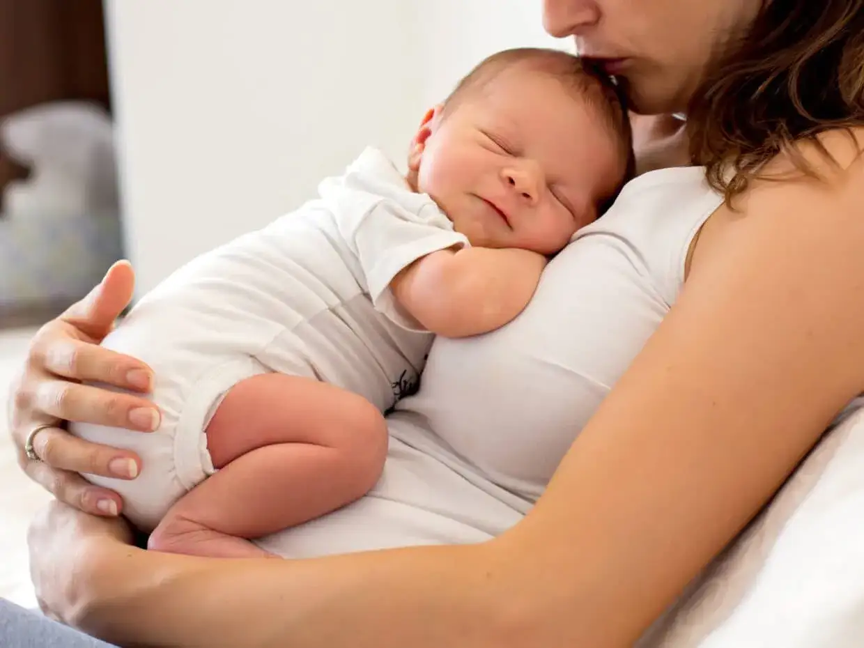Mamma bacia la fronte del suo neonato addormentato, un tenero esempio di quanto dormono i neonati.