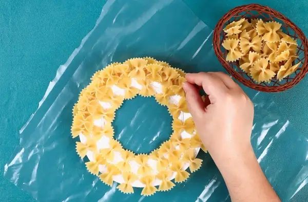 Mano che crea un lavoretto creativo per la festa della mamma con pasta a forma di farfalla su un cerchio di carta.