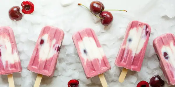 Ghiaccioli fatti in casa con ciliegie e yogurt, su un letto di ghiaccio tritato. Freschi e invitanti, perfetti per l'estate.