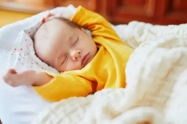 Dolce neonato piange nel sonno, avvolto in una coperta calda. Le sue braccia sono sollevate, come in un sogno agitato.
