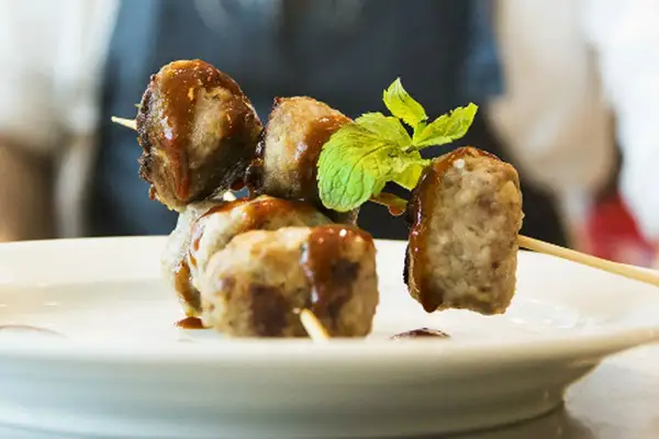 Spiedini di polpette di fagioli, condite con salsa e guarnite con menta fresca, su un piatto bianco.