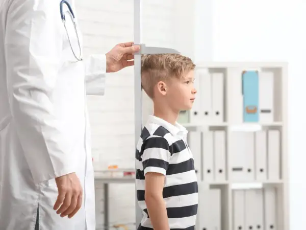 Un bambino viene misurato da un medico. La domanda "quanto sarà alto mio figlio" aleggia nell'aria mentre si attende il risultato.