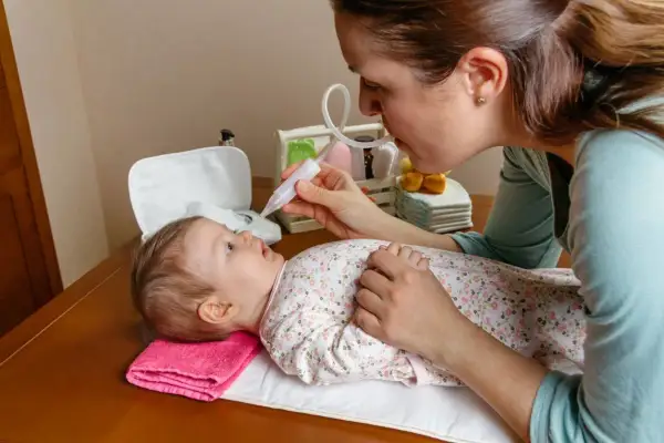 Mamma effettua lavaggi nasali a un neonato con un aspiratore nasale.