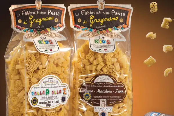 Due confezioni di pasta per bambini, una con lettere e l'altra con aerei, macchine e treni, prodotte a Gragnano.